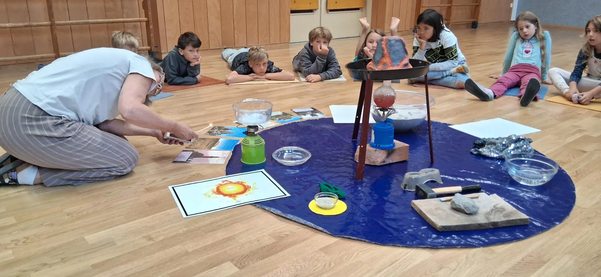 Eine Pädagogin begleitet eine kosmische Erzählung mit Vulkanmodell, während Kinder aufmerksam zuschauen