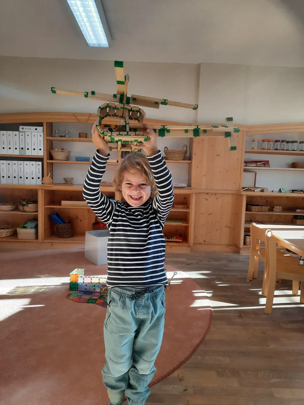 Ein Kindergartenkind hält stolz ein selbst gebautes Holzbauwerk hoch